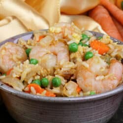 a bowl filled with shrimp fried rice next to a golden napkin on a silver tray