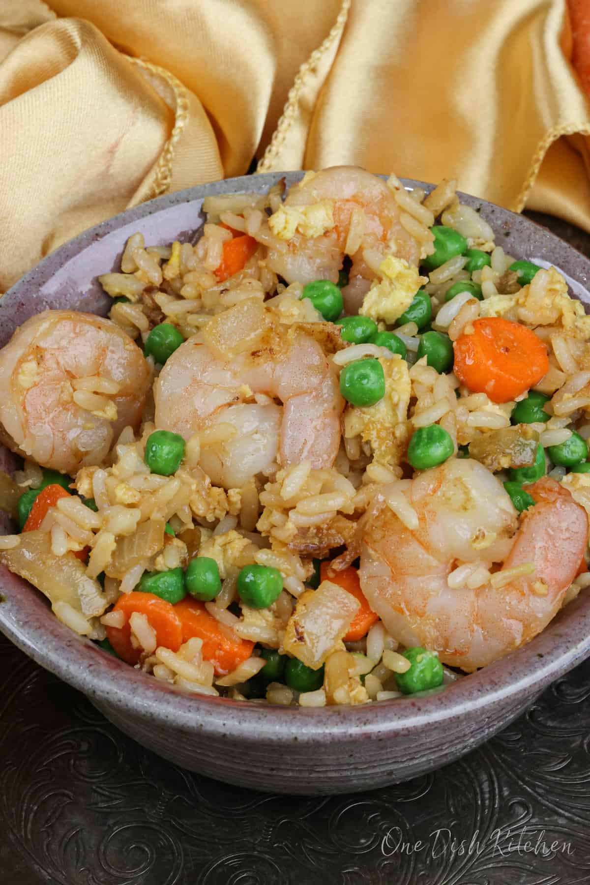 a bowl filled with shrimp fried rice next to a golden napkin on a silver tray.