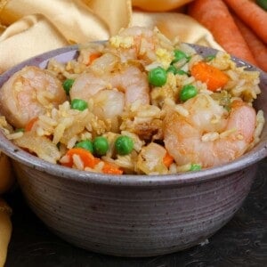 a bowl of shrimp fried rice next to three carrots and a gold napkin