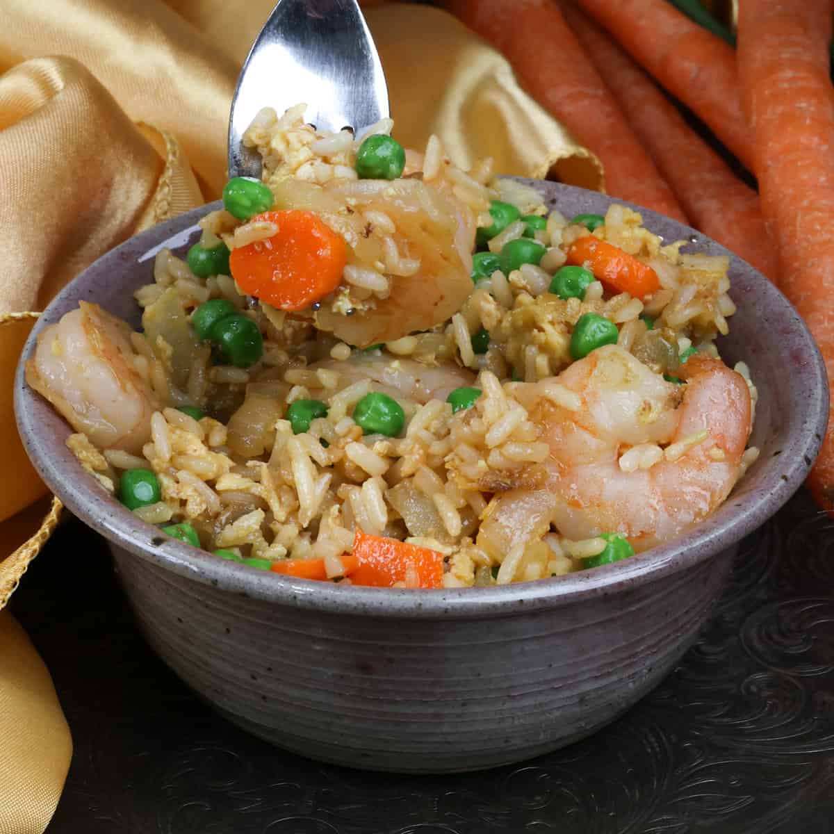 a fork filled with shrimp above a bowl of fried rice.