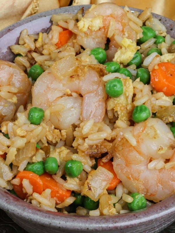 a bowl filled with shrimp fried rice next to a golden napkin on a silver tray