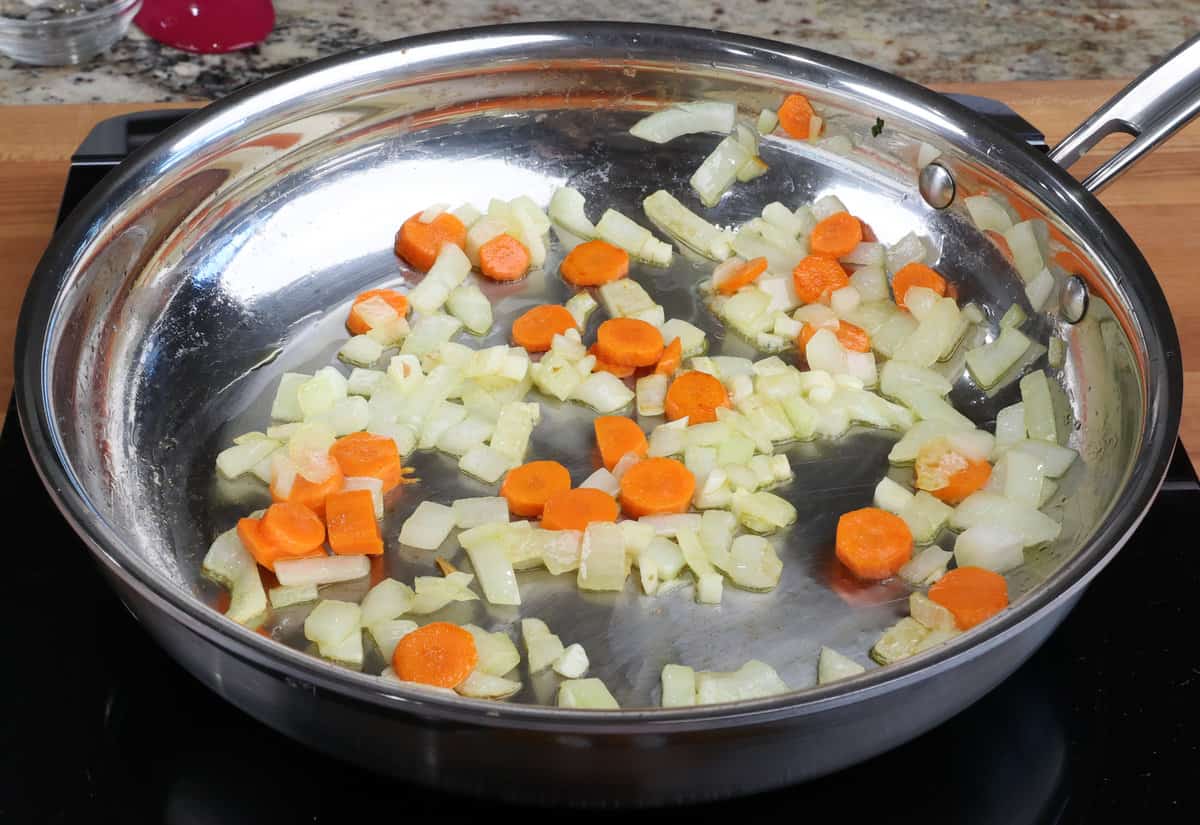 onions and carrots sauteeing in a skillet on the stove