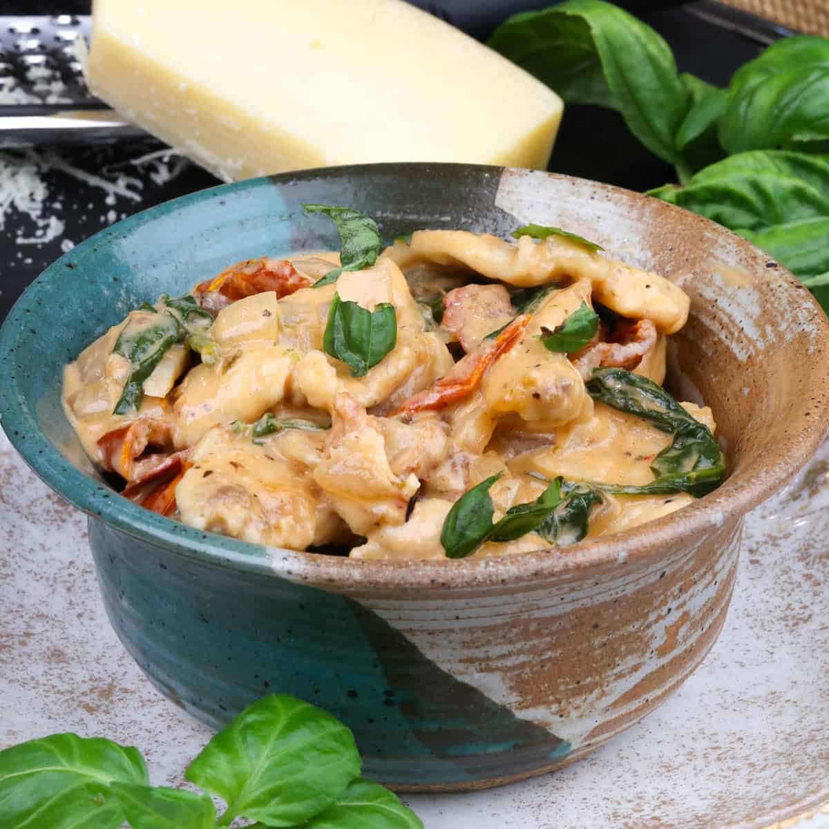 a small bowl of Tuscan chicken next to fresh basil and parmesan cheese wedges