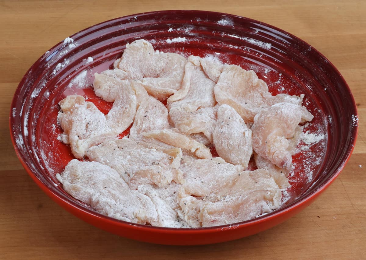 chicken pieces coated in flour in a red bowl.