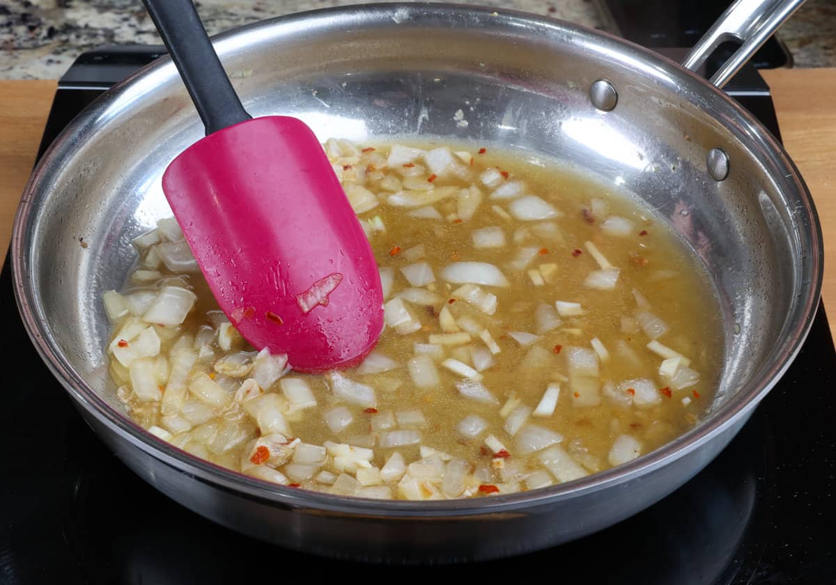 broth, onions, and garlic in a skillet with a rubber spatula stirring everything together