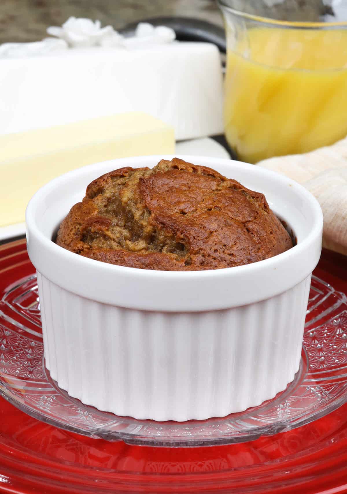 a small banana nut bread baked in a ramekin on a red plate next to a plate of butter and a glass of orange juice