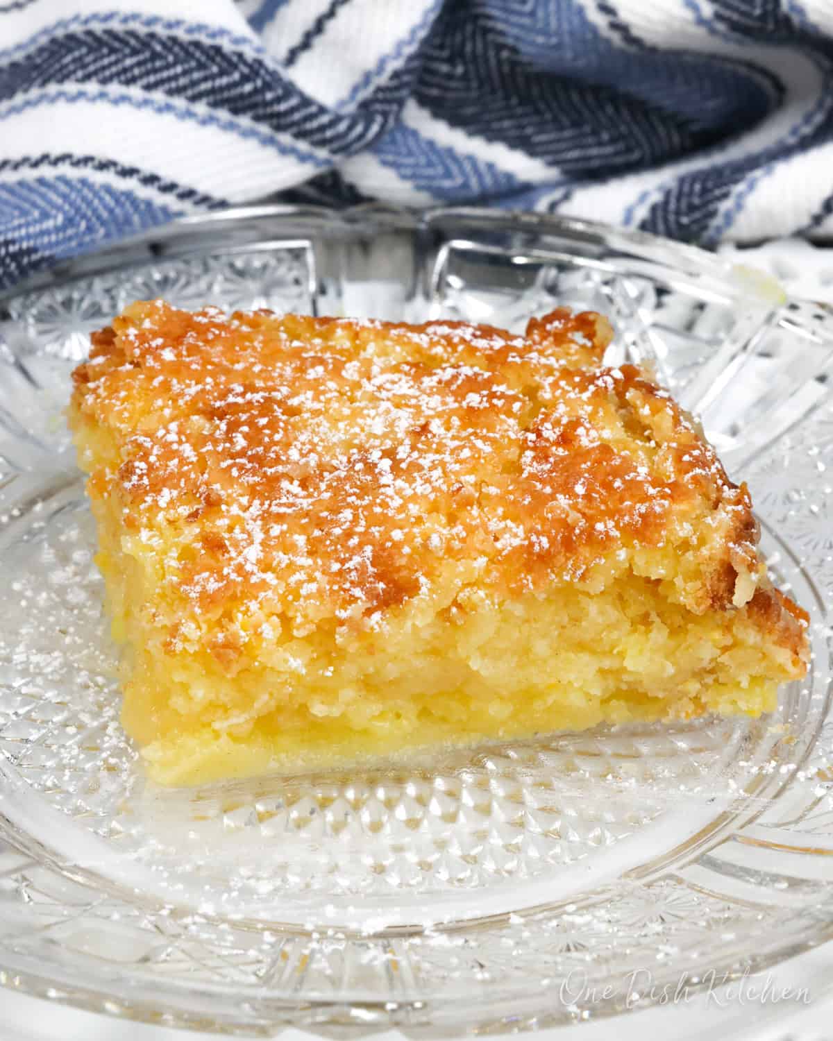a slice of chess pie on a white plate next to a blue and white striped napkin.