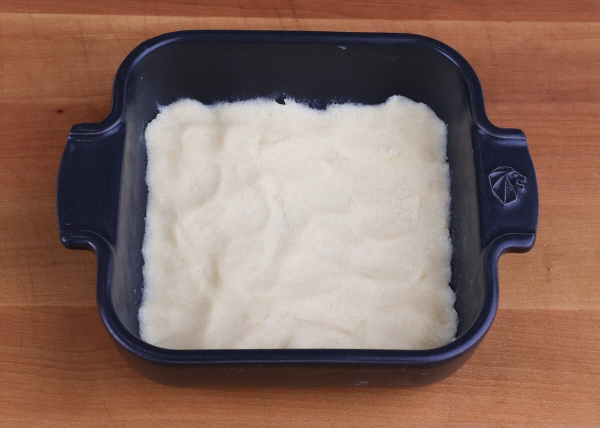 pie crust pressed into a small square baking dish on a wooden table.