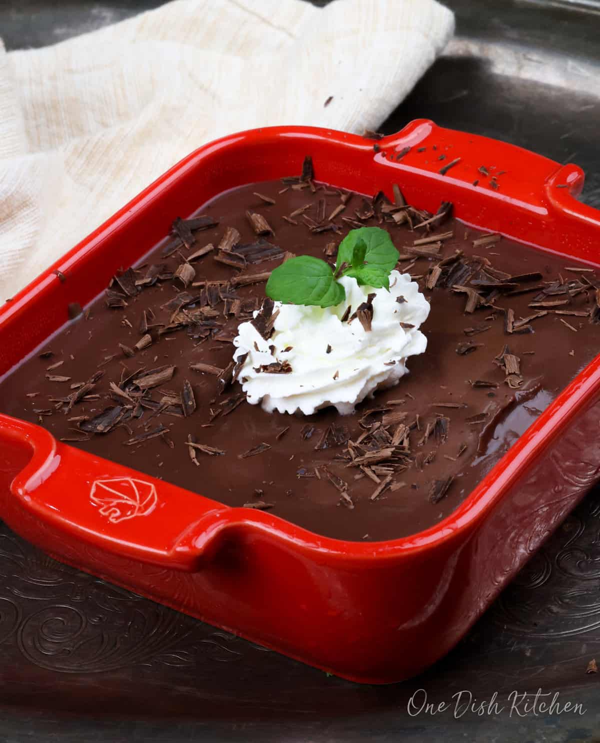 a mini chocolate pie in a red square baking dish topped with whipped cream and fresh mint.