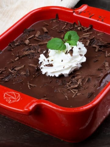 a mini chocolate pie in a red square baking dish topped with whipped cream and fresh mint
