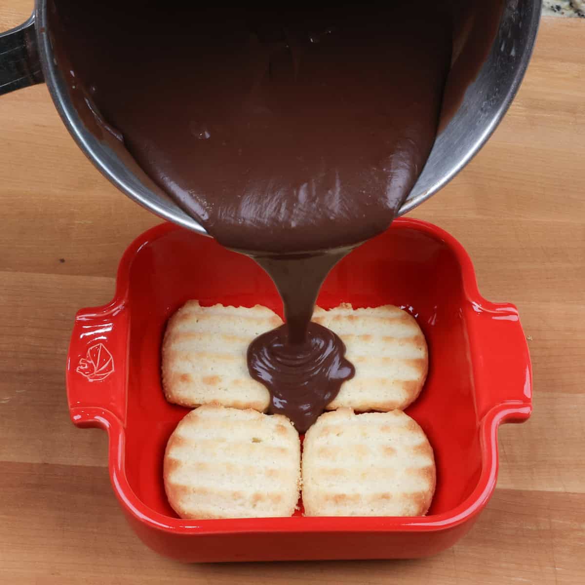 four cookies lining a small red baking dish with chocolate pudding poured over the top.