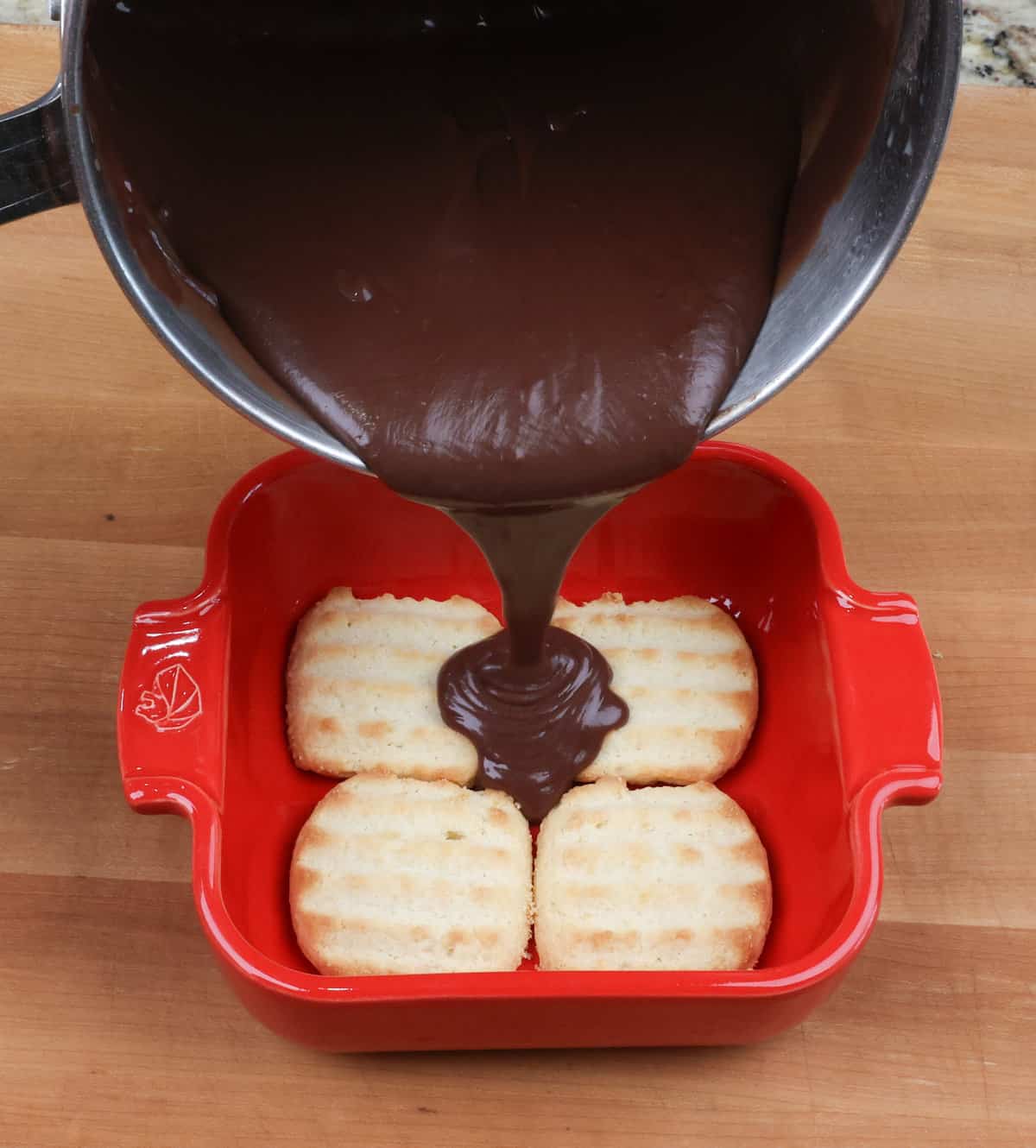 Pouring homemade chocolate pudding over cookies in a baking dish to make a chocolate pie.