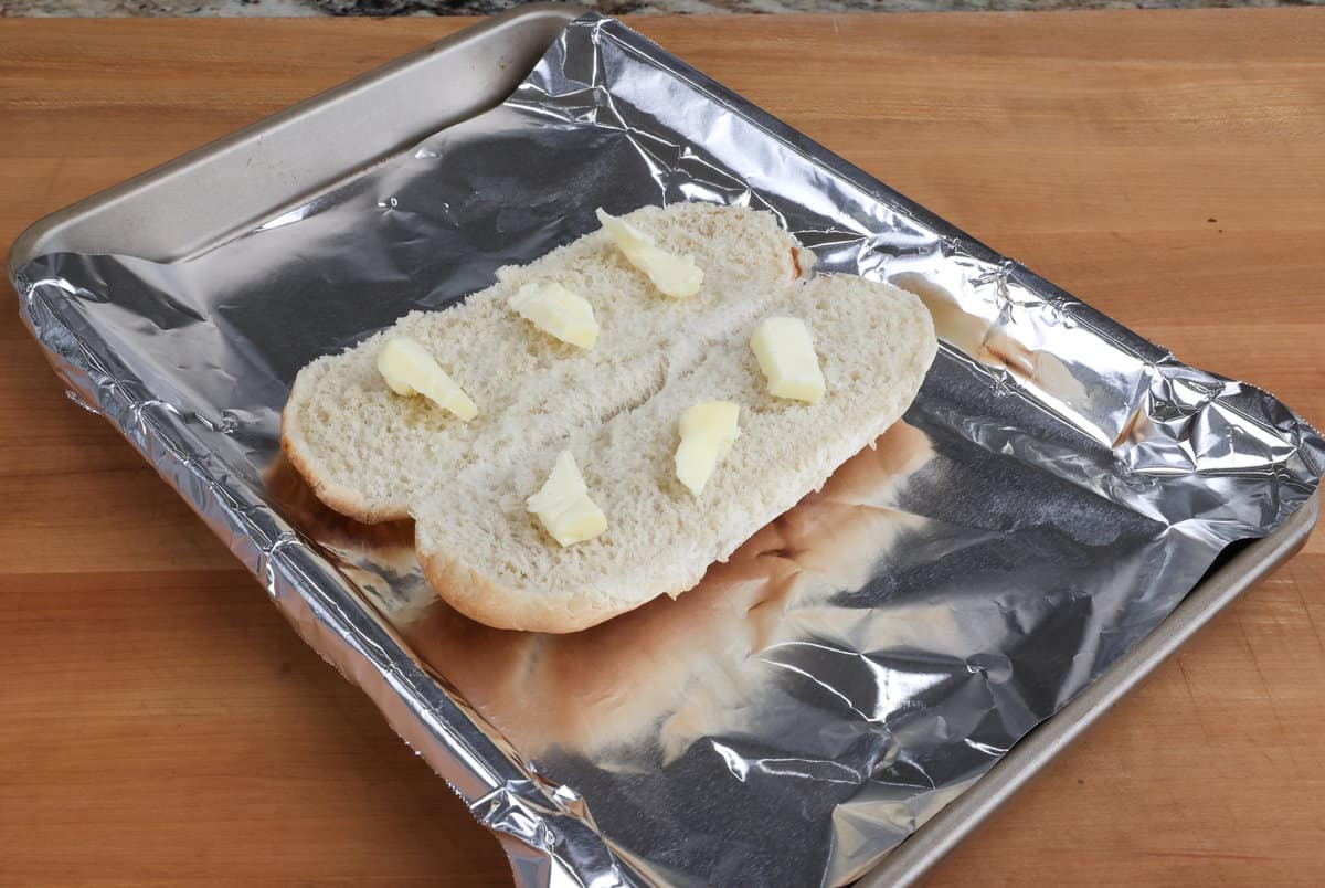 butter on a hoagie roll sitting on a baking sheet.
