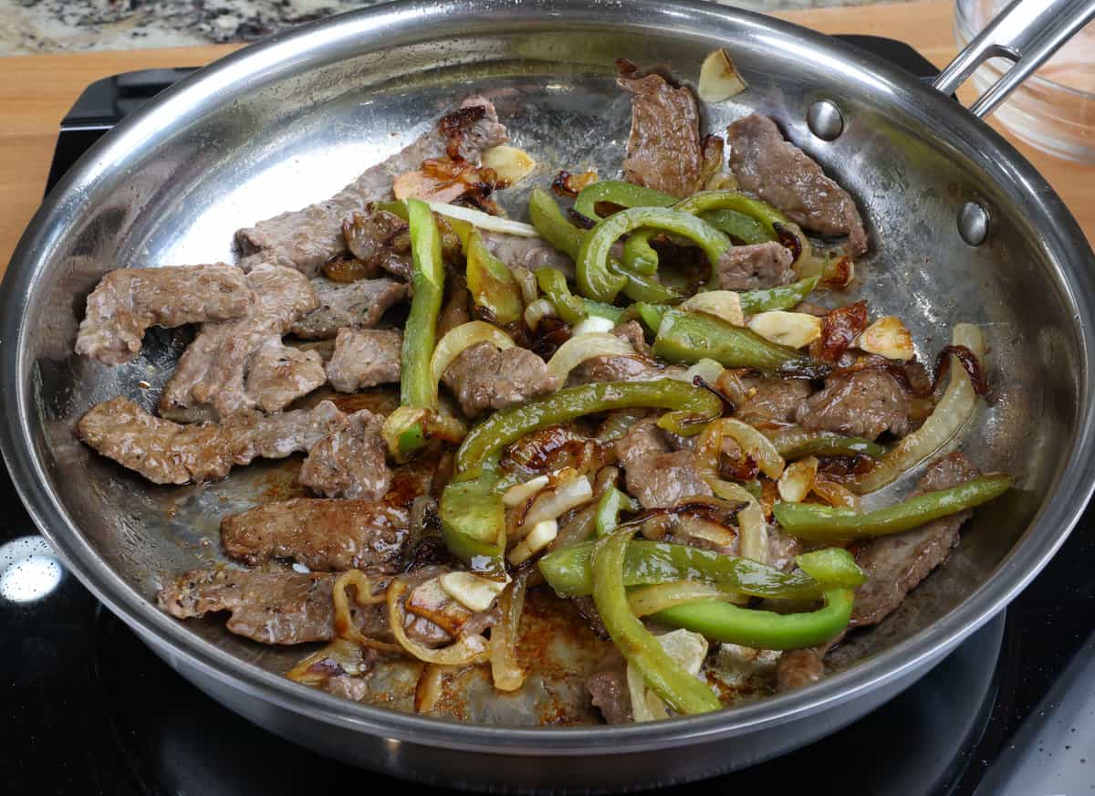 steak, peppers, and onions cooking together in a large skillet