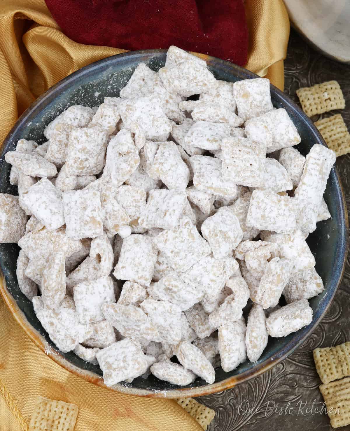 an overhead view of a bowl of muddy buddies made with white chocolate chips on a silver tray