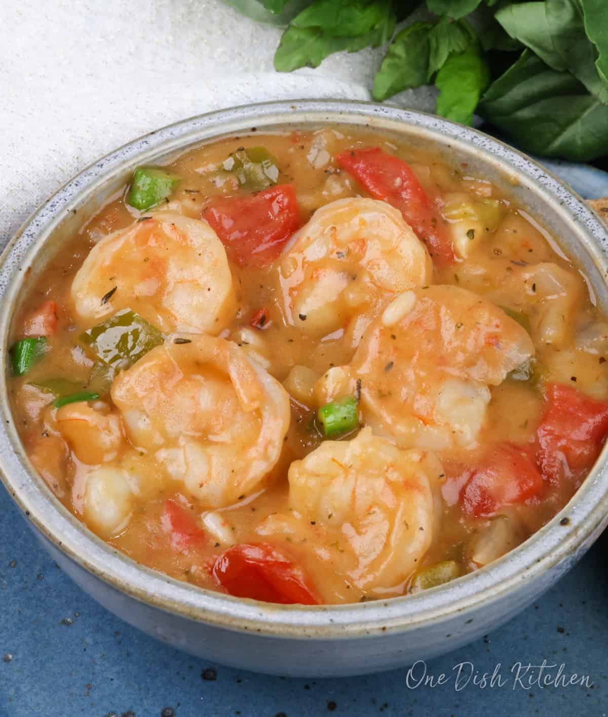 a blue bowl filled with shrimp etouffee next to a white napkin.