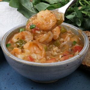a bowl of shrimp etouffee with a spoon above the bowl holding a shrimp