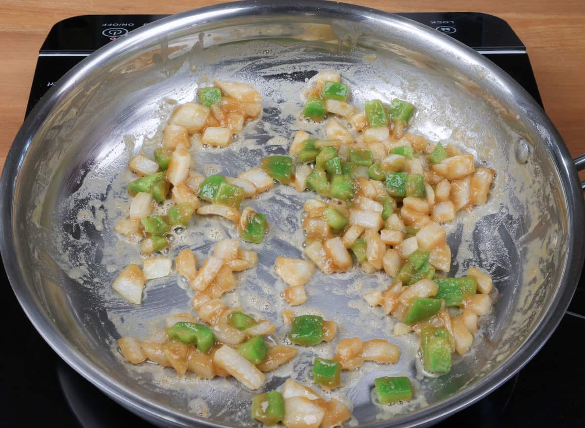 onions and green bell peppers cooking in a roux in a skillet
