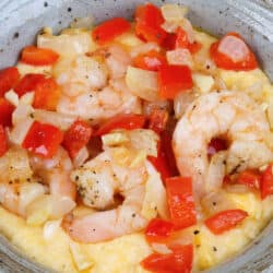 an overhead view of shrimp, onions, garlic and red peppers on top of cheese grits