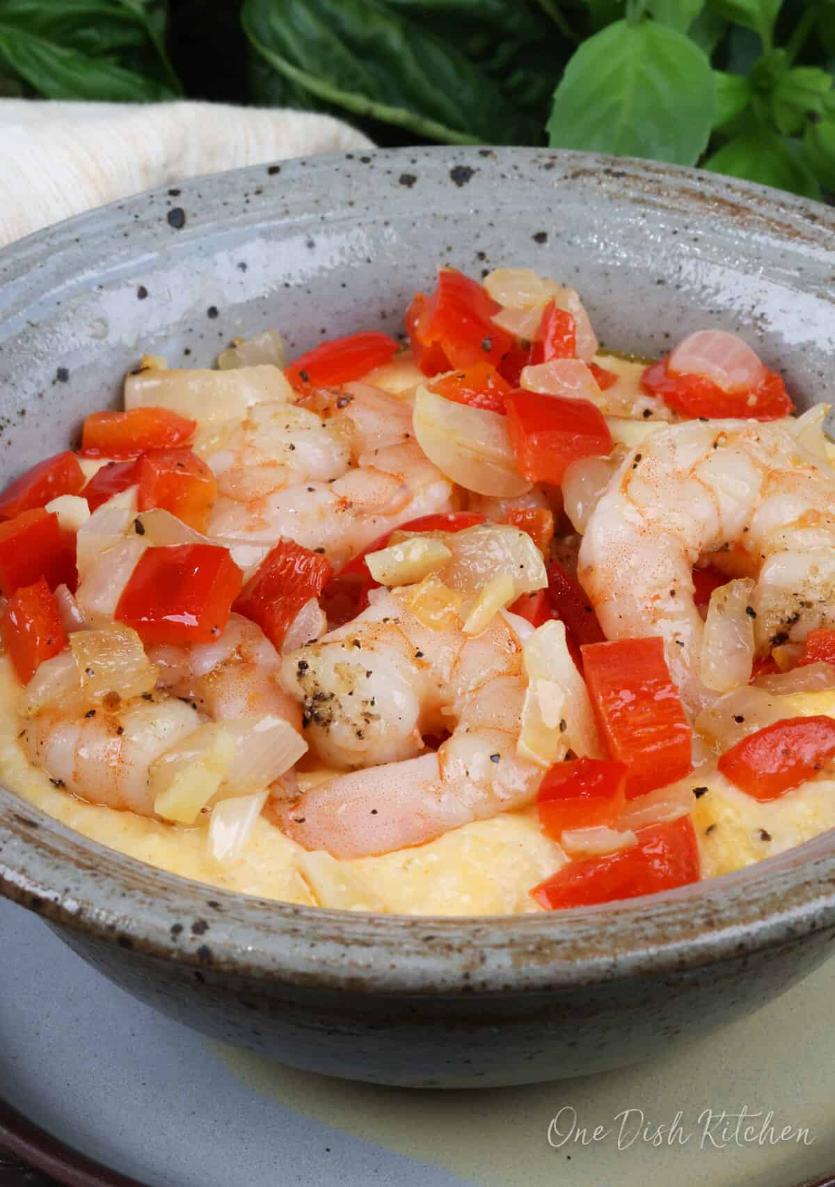 a bowl of shrimp and grits topped with onions and red bell peppers next to fresh basil