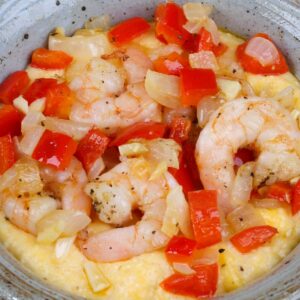 a bowl of shrimp and grits topped with onions and red bell peppers.