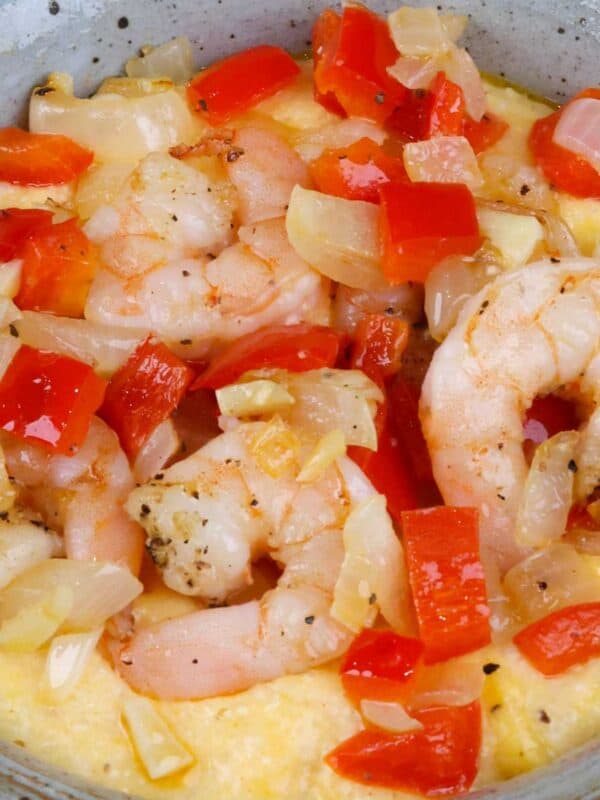 a bowl of shrimp and grits topped with onions and red bell peppers.
