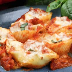six jumbo pasta shells stuffed with ricotta and mozzarella cheese on a blue plate next to a red napkin