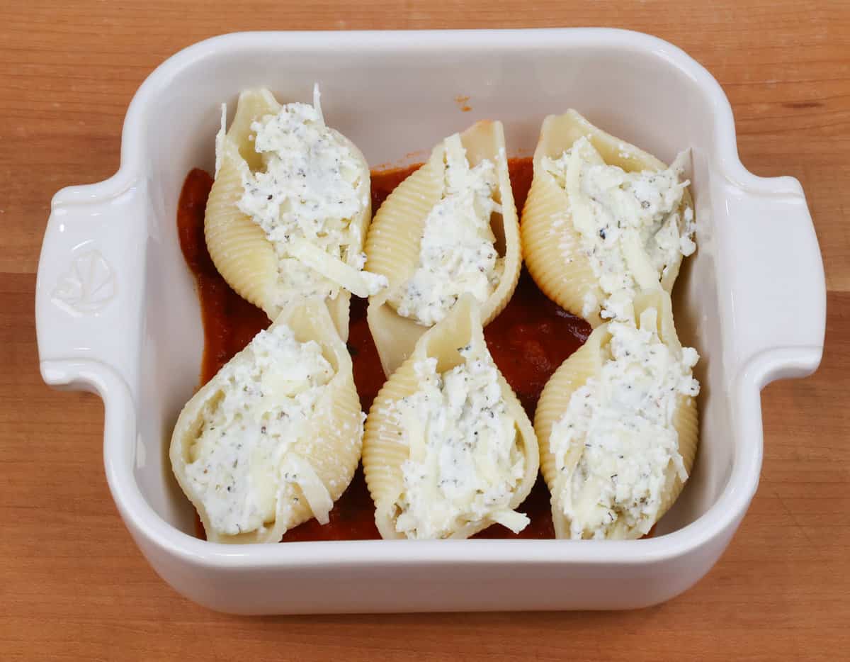 six unbaked stuffed pasta shells in a small square baking dish