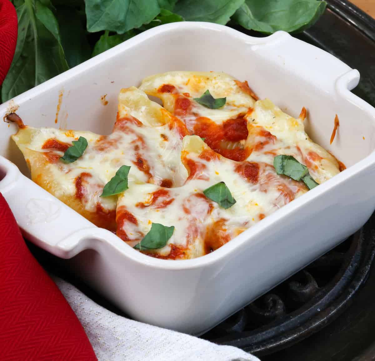 baked pasta shells in a white square baking dish topped with fresh basil.