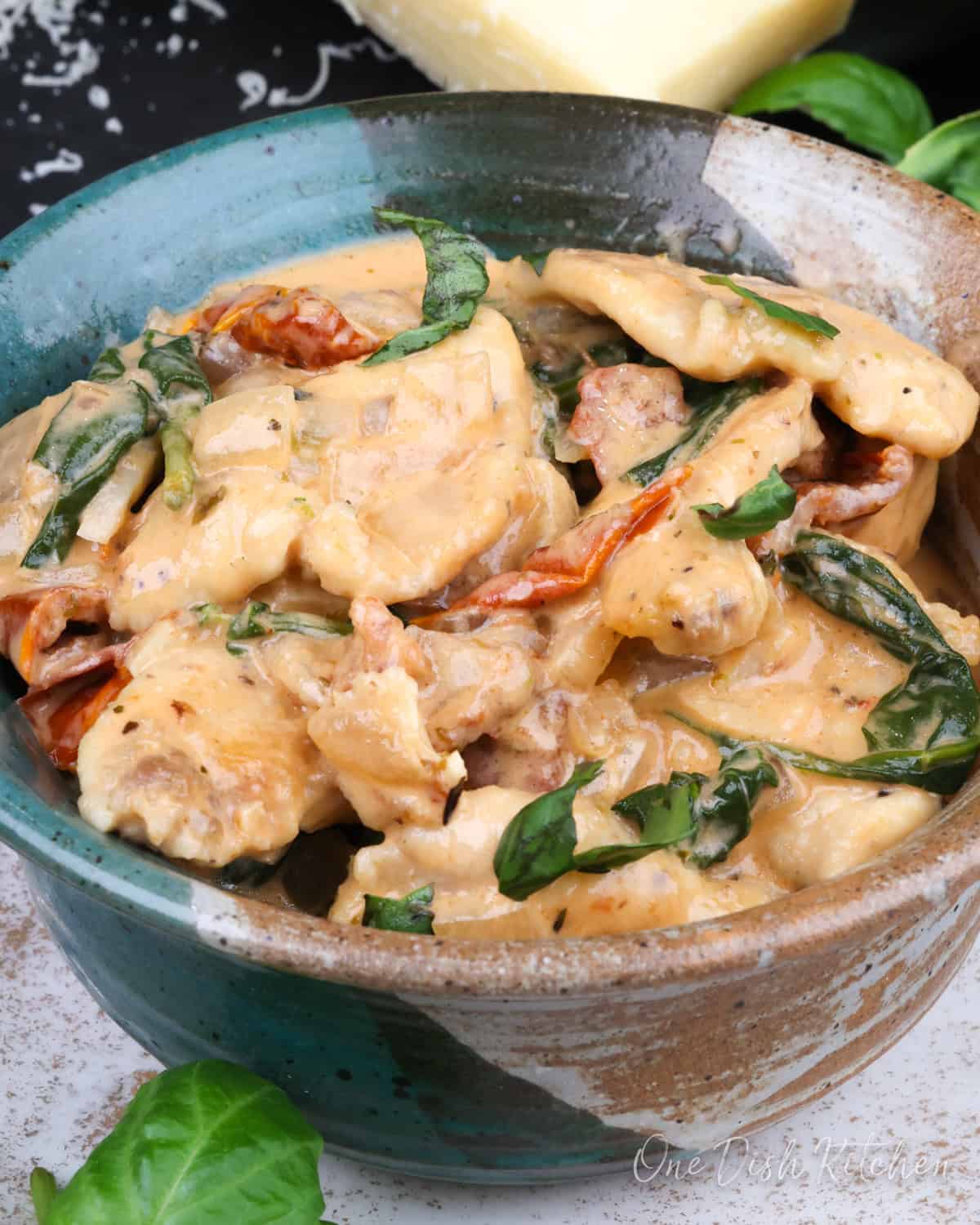 a bowl of tuscan chicken next to a wedge of Parmesan cheese.