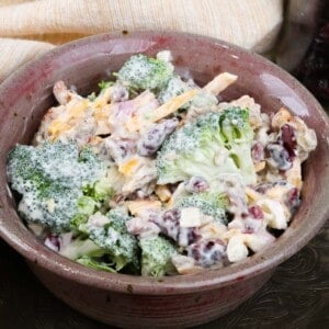 broccoli salad with shredded cheese, seeds, broccoli florets and dried fruit in a small bowl next to a beige napkin