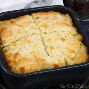 a small square baking dish filled with 4 butter swim biscuits next to a white napkin and a jar of jelly.
