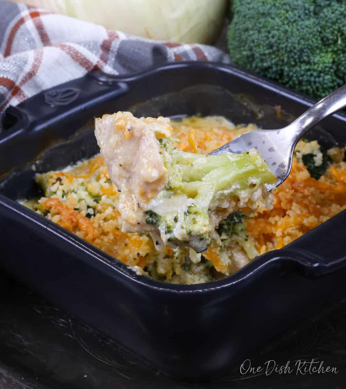 a fork filled with chicken and broccoli over a small dish of chicken divan