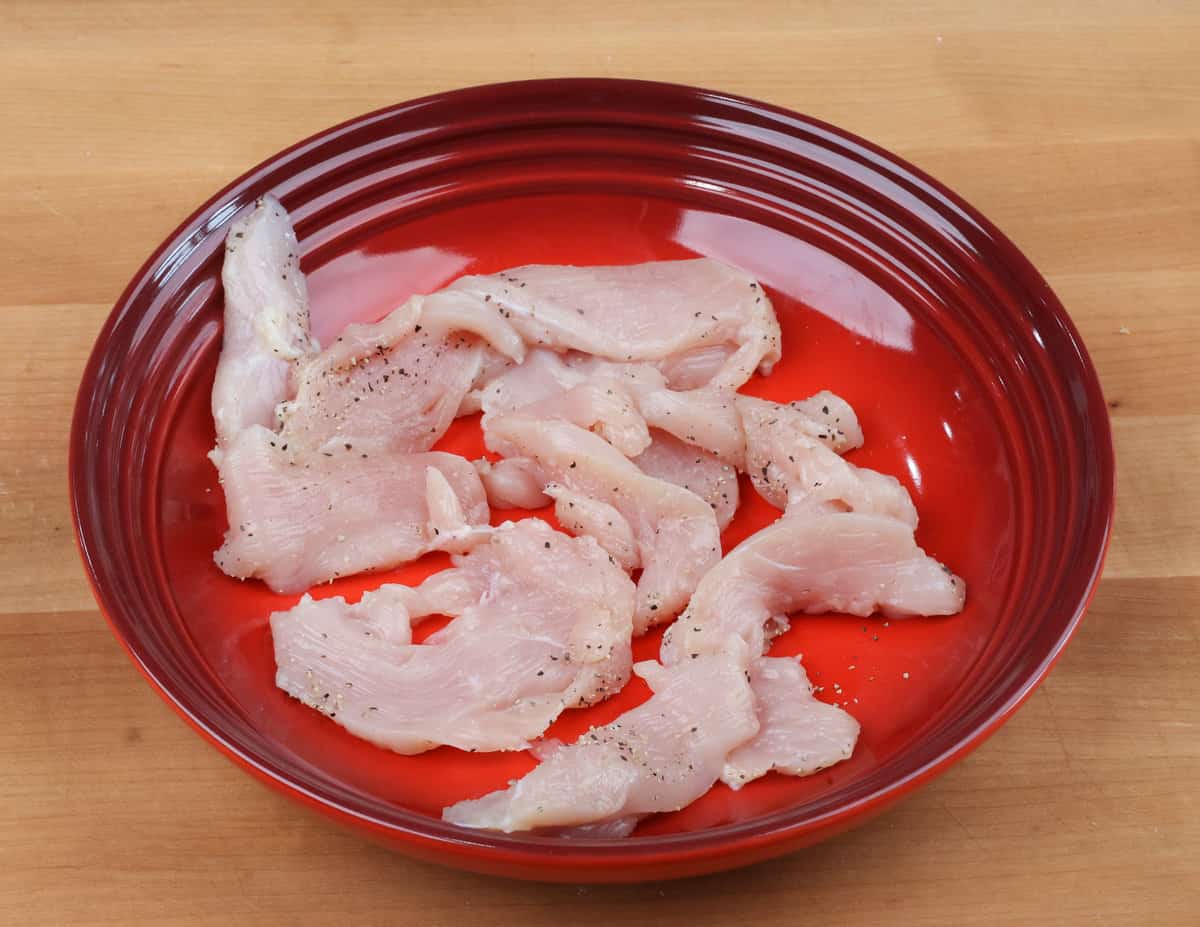slices of raw chicken seasoned with salt and pepper in a red bowl