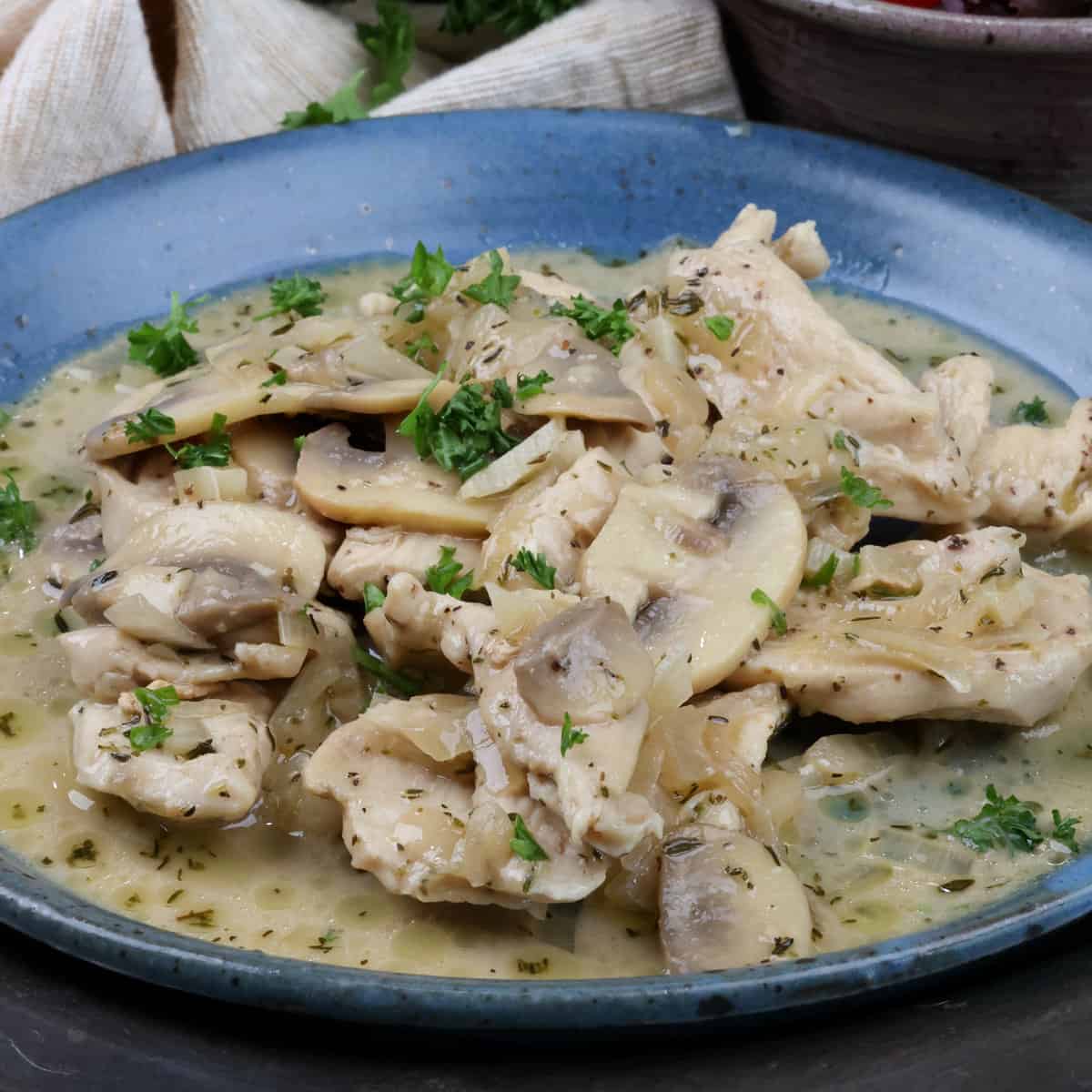 a low carb chicken marsala on a blue plate topped with chopped parsley