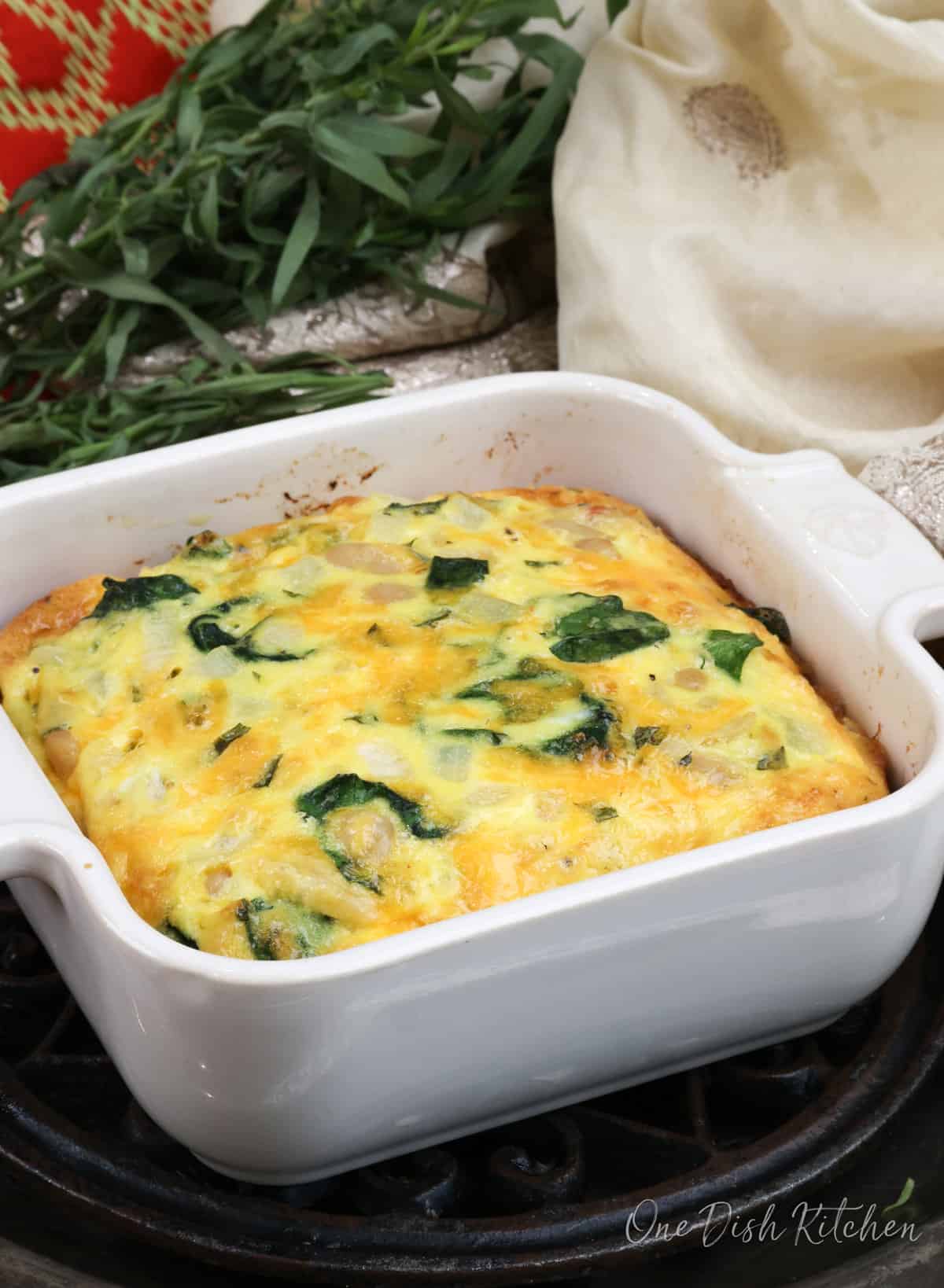 a small coronation quiche baked in a white square baking dish next to fresh tarragon