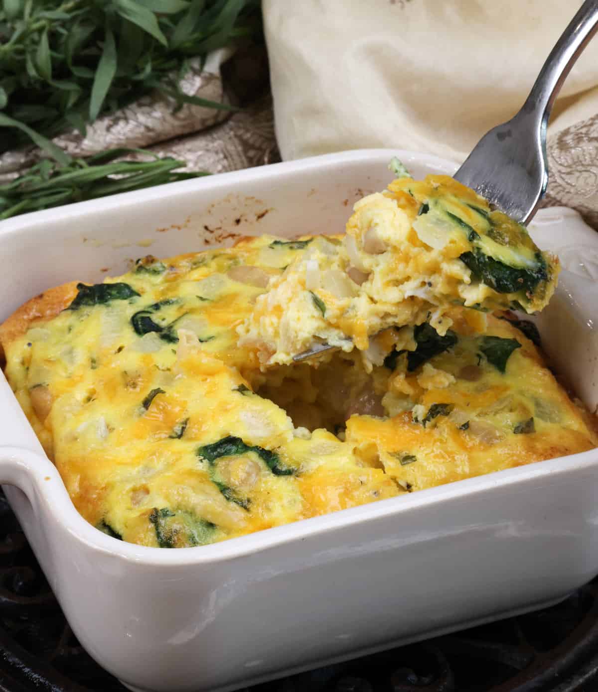 a fork above a coronation spinach quiche on a silver tray