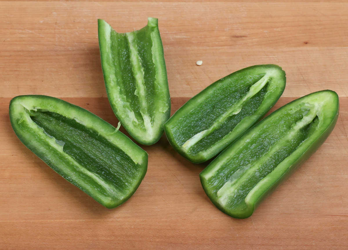 four halves of two jalapenos on a wooden cutting board with the membranes and seeds removed.