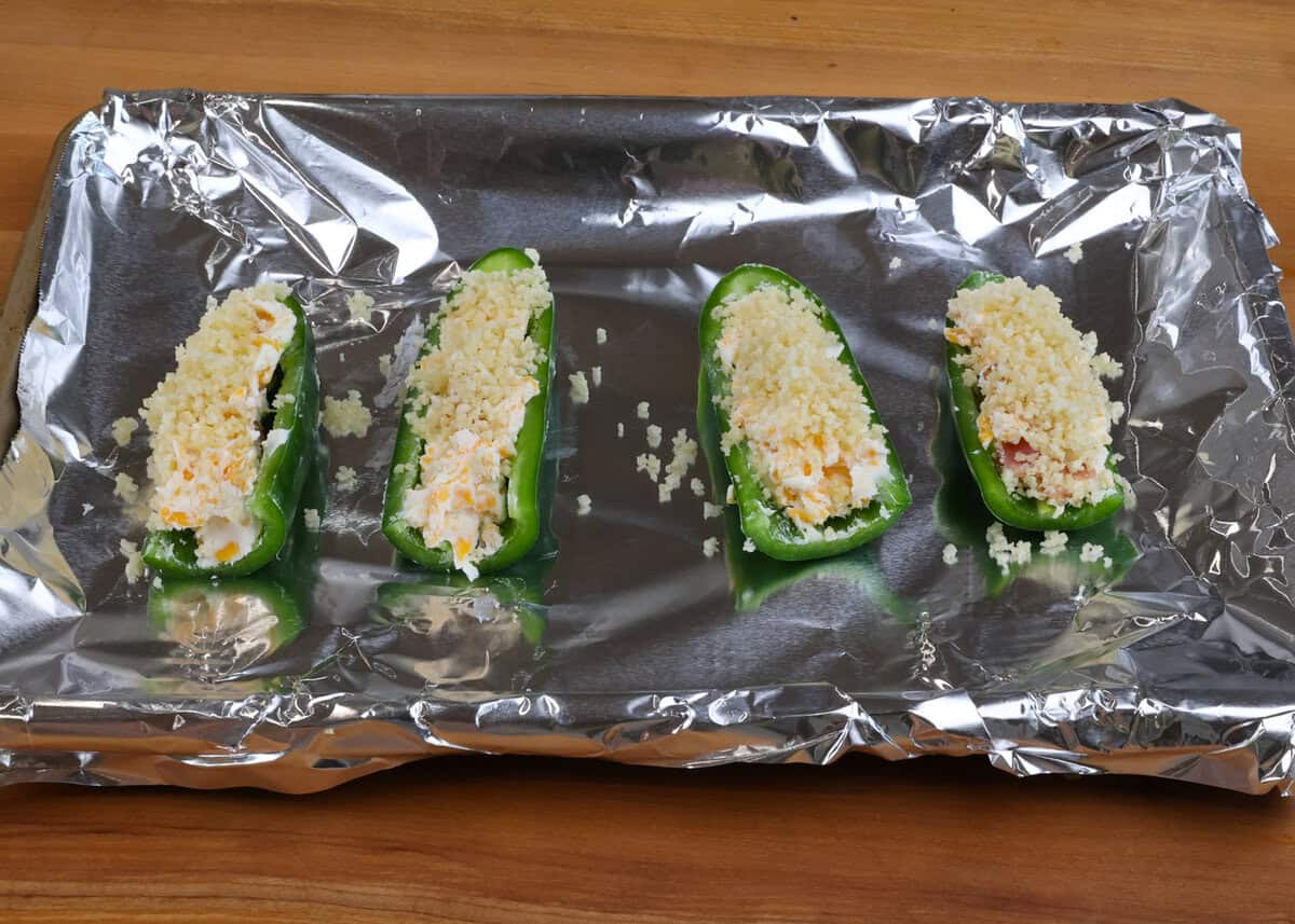four unbaked jalapeno poppers on a baking sheet.