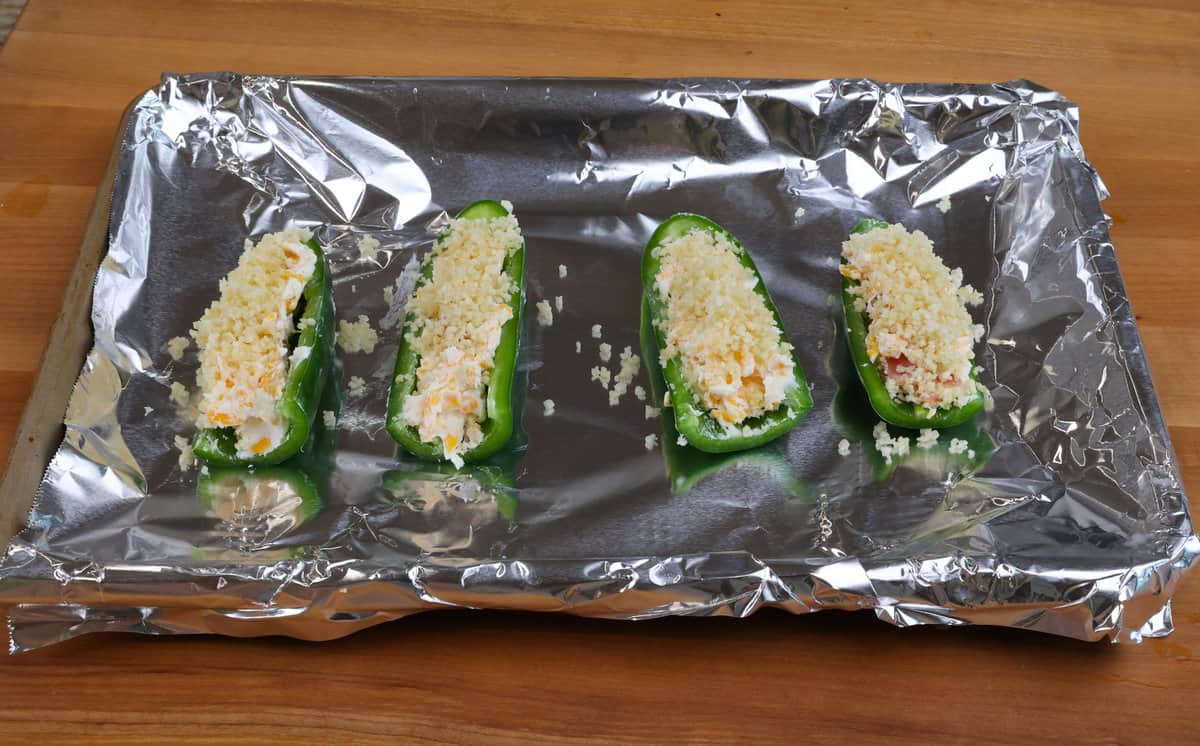 four unbaked jalapeno poppers on a baking sheet
