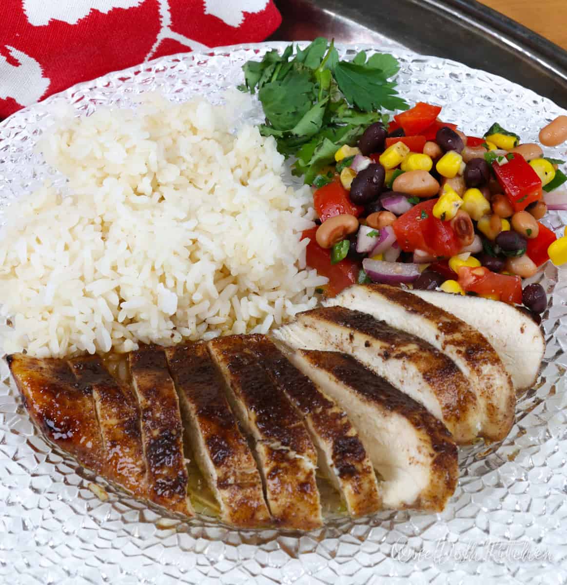 jerk chicken breast on a white plate next to white rice and vegetable salad.