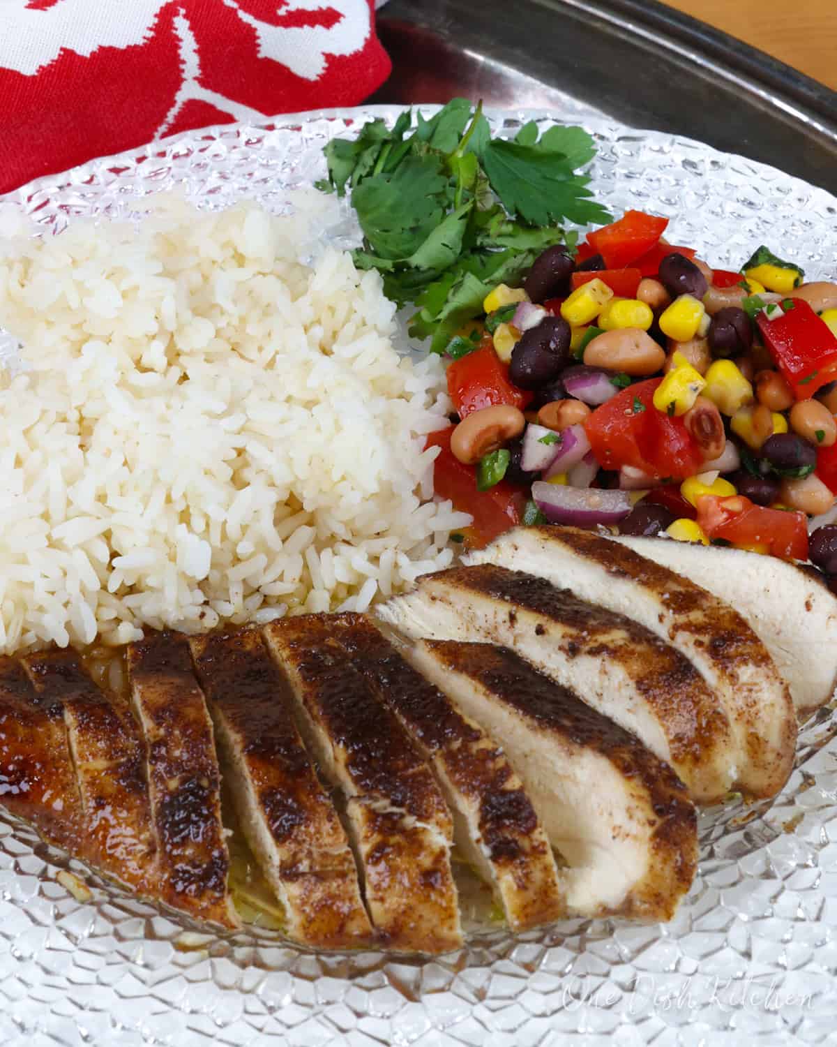 jerk chicken breast on a white plate next to white rice and vegetable salad.
