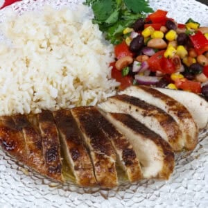jerk chicken breast on a white plate next to white rice and vegetable salad.