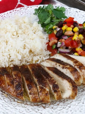jerk chicken breast on a white plate next to white rice and vegetable salad