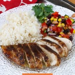 Jamaican Jerk Chicken sliced on a plate next to rice and vegetables.