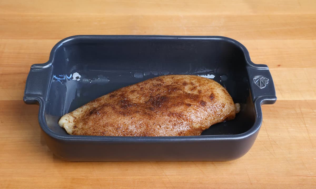 an uncooked chicken breast seasoned with jerk seasoning in a small baking dish.
