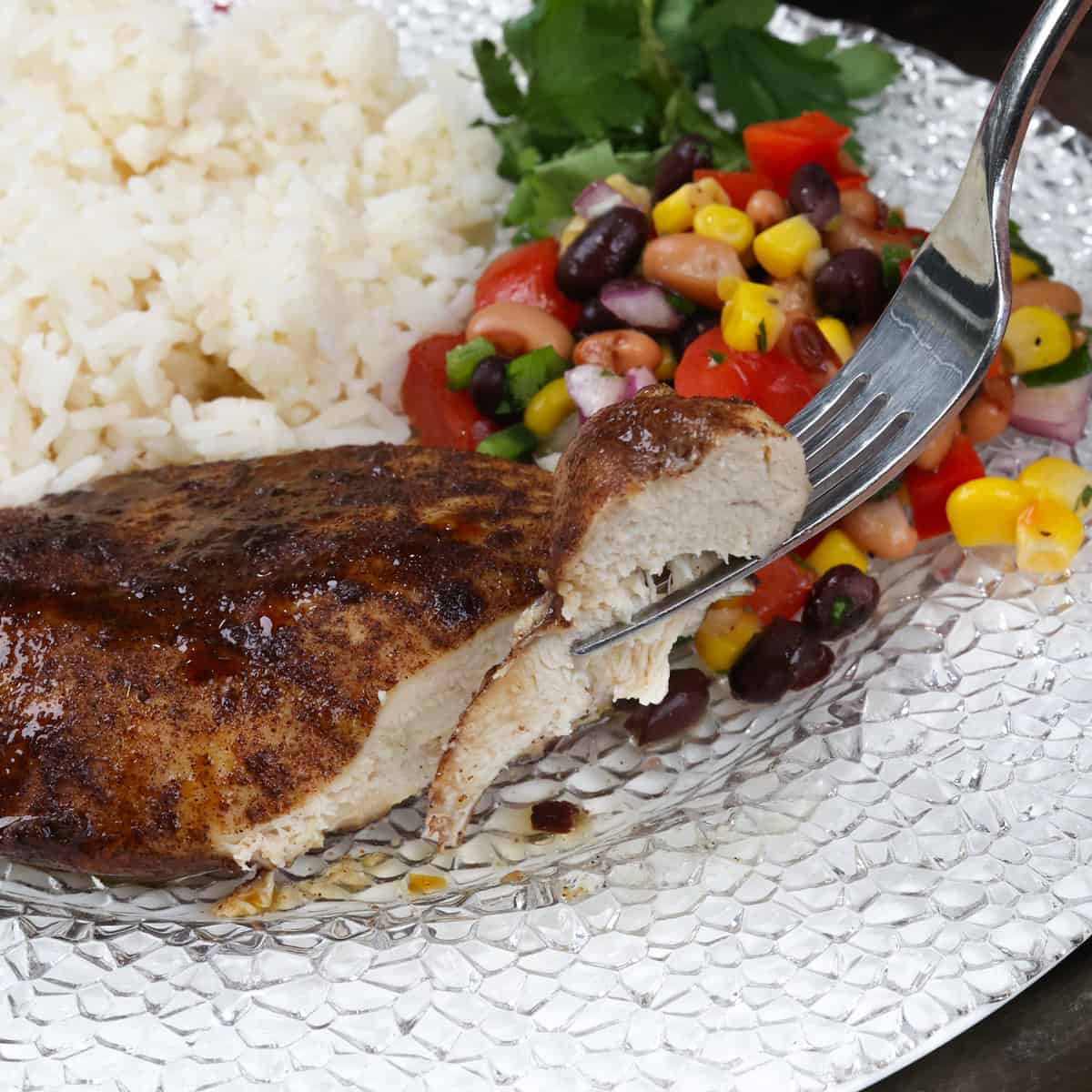 sliced jerk chicken on a plate with white rice and corn salad on the side.