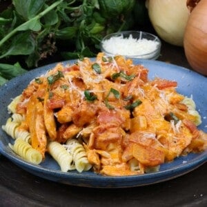 chicken with paprika sauce over rotini pasta next to fresh basil and a bowl of grated parmesan cheese