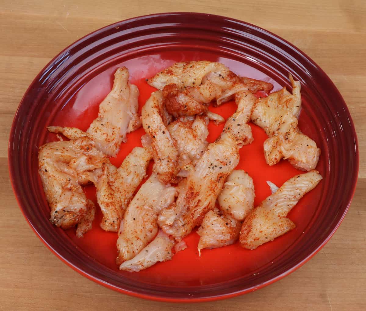 chicken pieces seasoned with paprika in a red bowl.