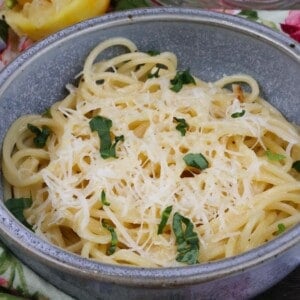 pasta al limone in a blue bowl topped with shredded parmesan cheese and chopped fresh basil